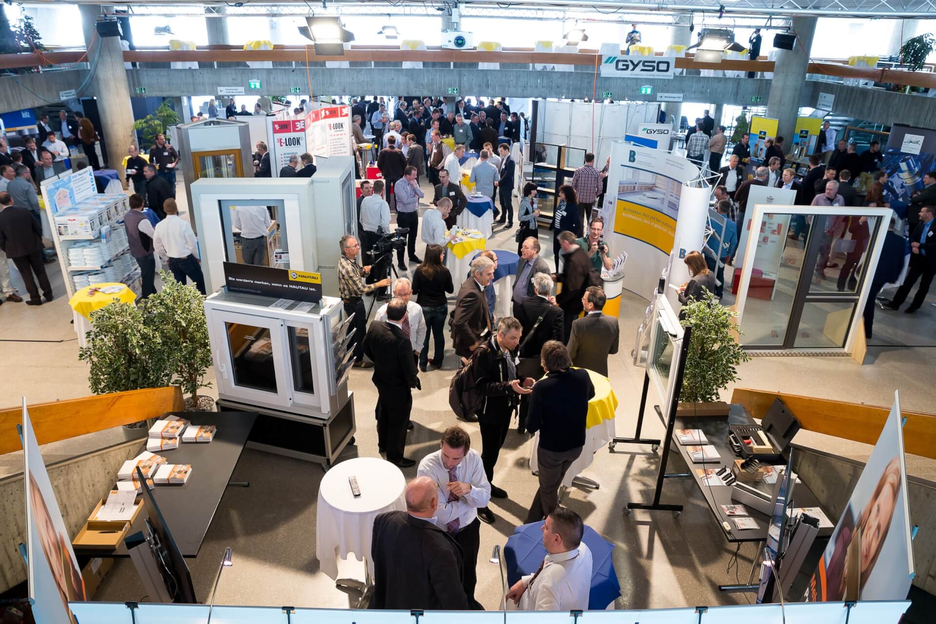 Eine geschäftige Messe mit zahlreichen Besuchern, Ständen und Produktausstellungen in einer großen Halle. Die Menschen tauschen sich aus und knüpfen Kontakte rund um die verschiedenen Ausstellungsstücke.