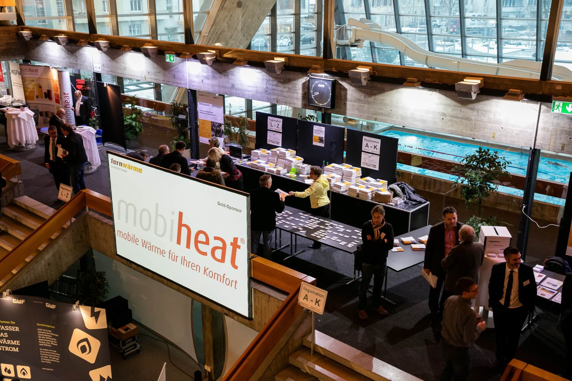 Ausstellungshalle mit Menschen, die an Ständen Kontakte knüpfen, Informationsdisplays und einem großen 