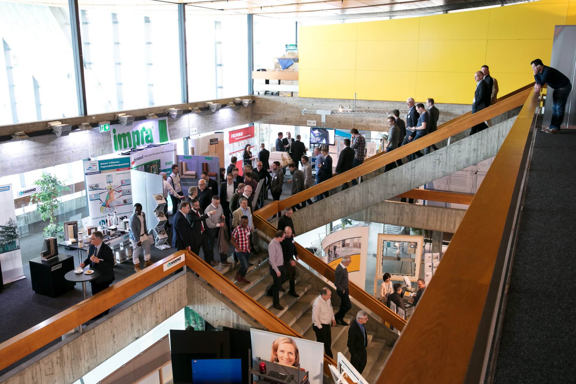 In einem mehrstöckigen überdachten Veranstaltungsraum mit Informationsplakaten und Ständen auf beiden Etagen laufen die Menschen um die Exponate herum und versammeln sich.