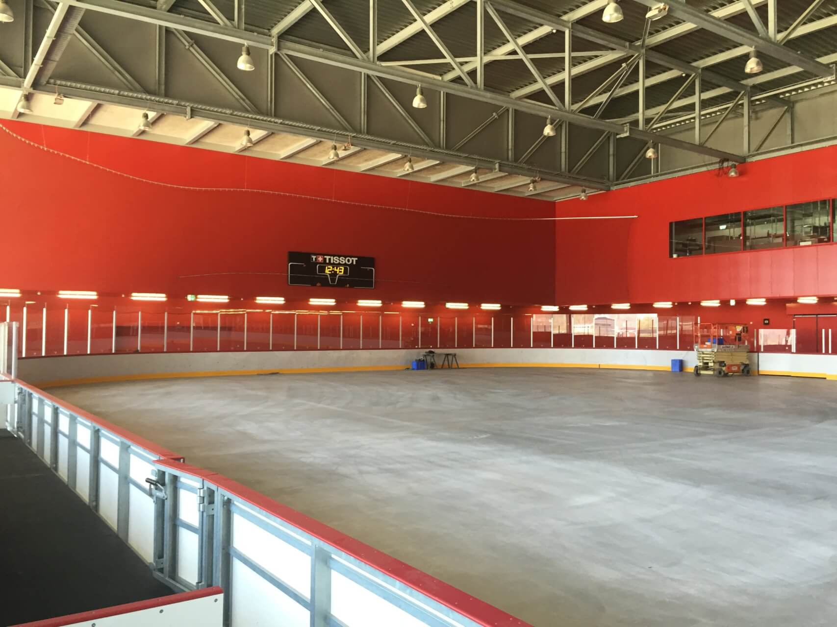 Eine Eishockeyhalle ohne Eis, mit Betonboden, roten Wänden, leeren Sitzplätzen und einer Anzeigetafel über der Halle.