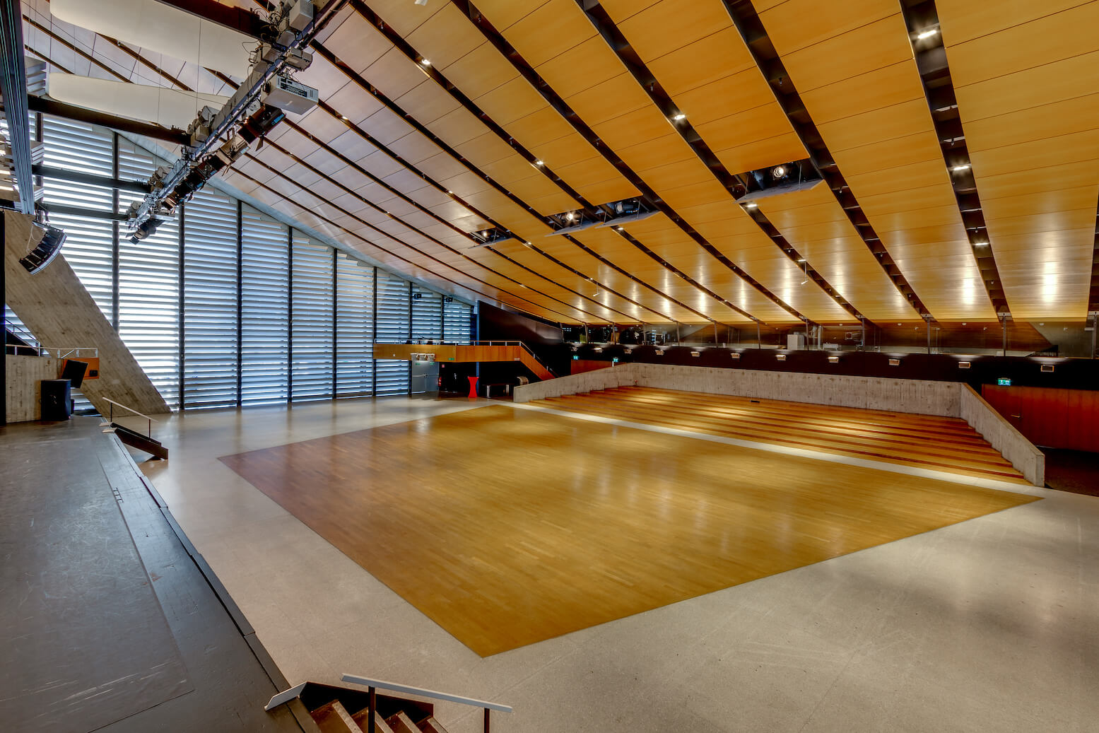 Weitwinkelansicht eines modernen Auditoriums mit abgestufter Bestuhlung, einem großen Holzboden und einer Decke mit Holzverkleidung und Beleuchtungskörpern.