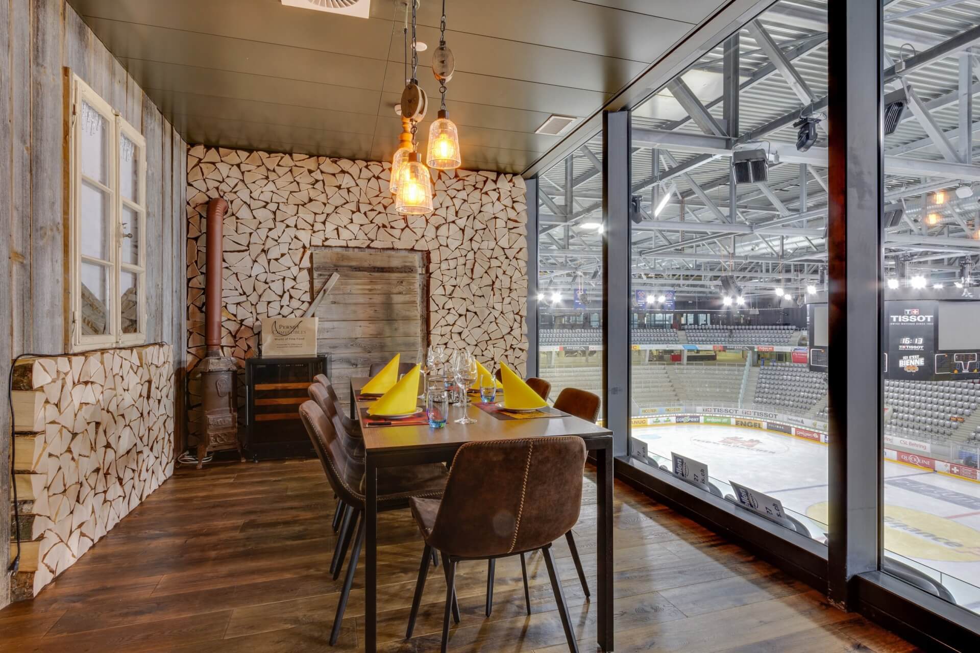 Ein moderner Essbereich mit rustikalem Holzdekor bietet durch große Glasfenster einen Blick auf eine leere Eishockey-Arena.