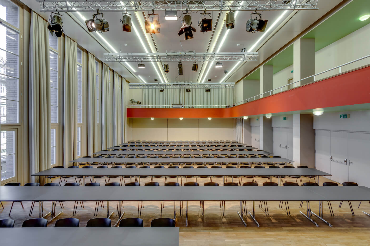 Großer, moderner Hörsaal mit langen Tischen und schwarzen Stuhlreihen, hohen Decken, großen Fenstern und Deckenbeleuchtung.