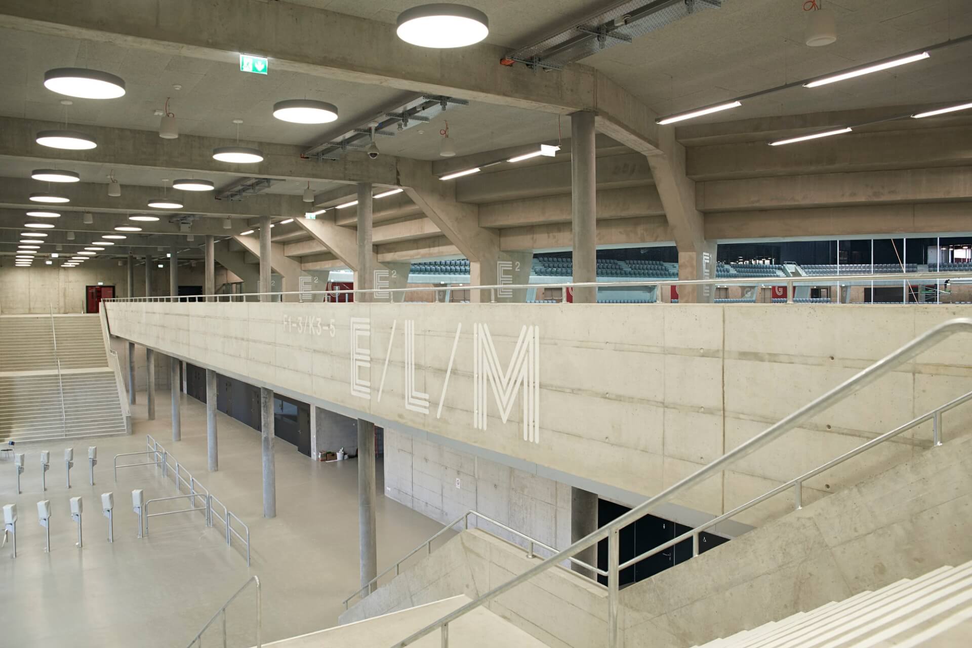 Ein moderner, geräumiger Innenbereich mit Sichtbetonwänden, hohen Decken und großen runden Oberlichtern; Metallgeländer und Treppen sind sichtbar.