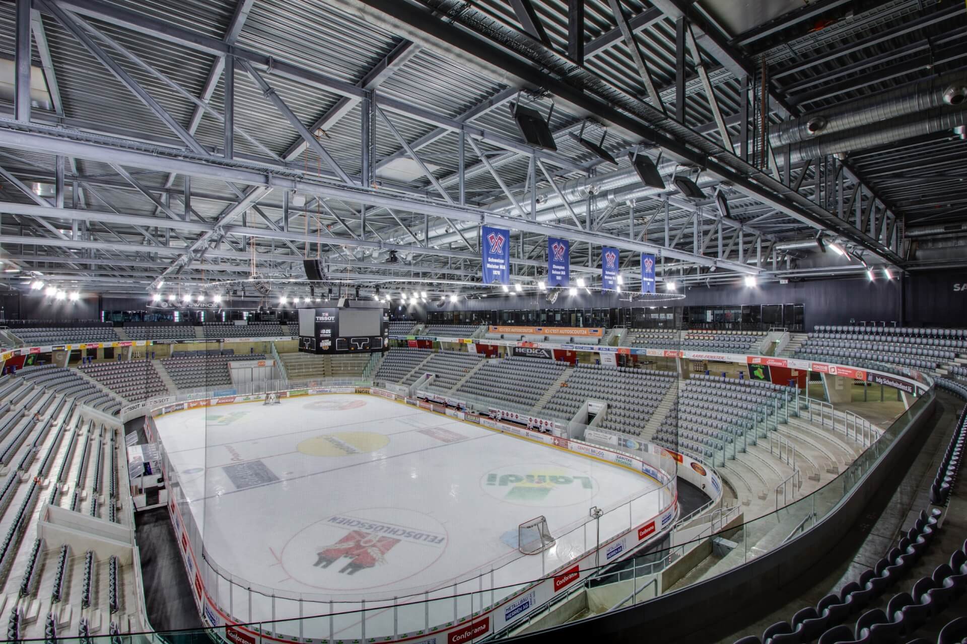Eine leere Eishockeyhalle mit markierter Eisfläche, umliegenden Sitzplätzen, Bannern und Oberlichtern, von einem Ende über der Tribüne aus gesehen.
