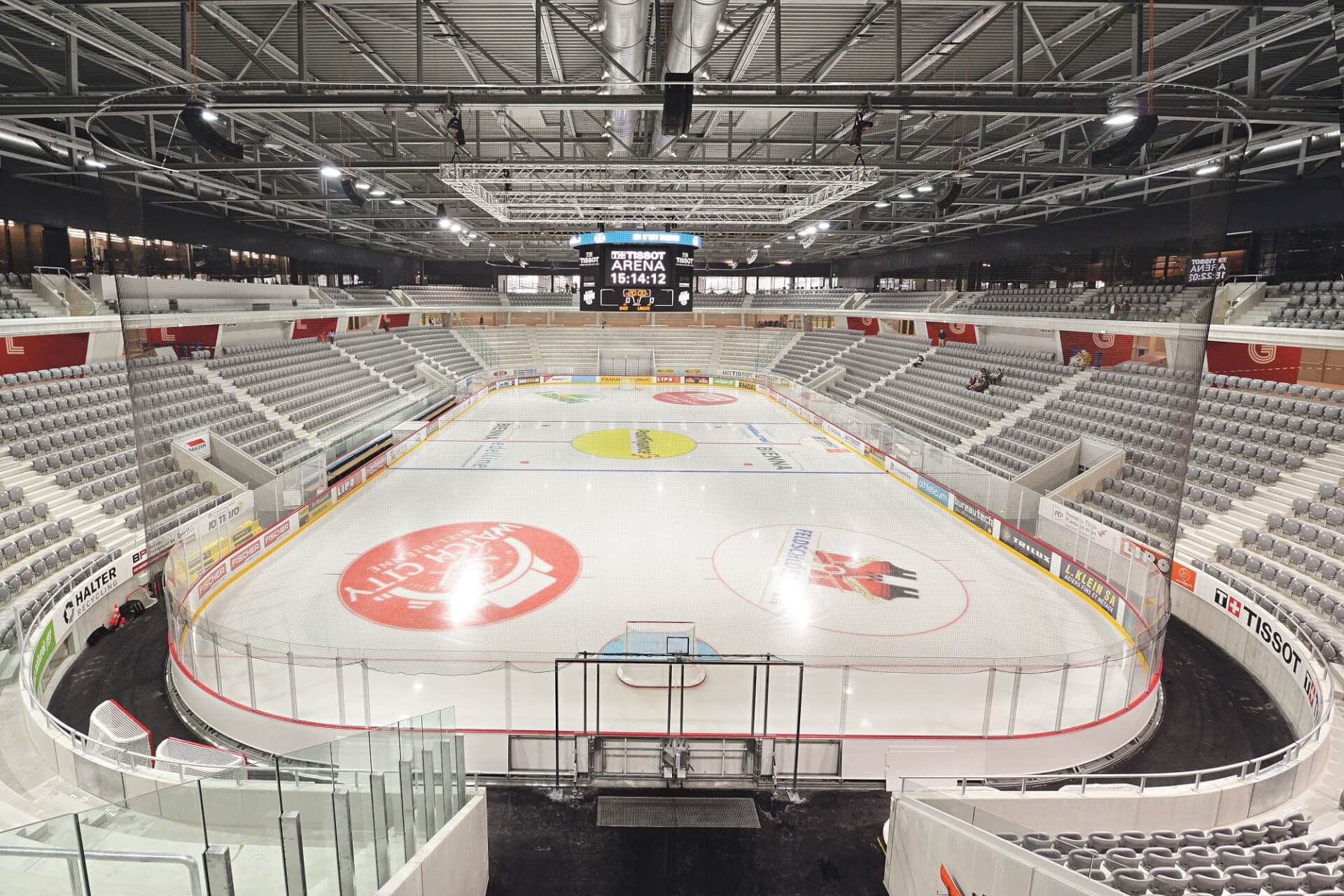 Leere Eishockeyhalle mit übersichtlicher Eisfläche, Sitzplätzen auf allen Seiten und einer großen Anzeigetafel über der Eismitte.