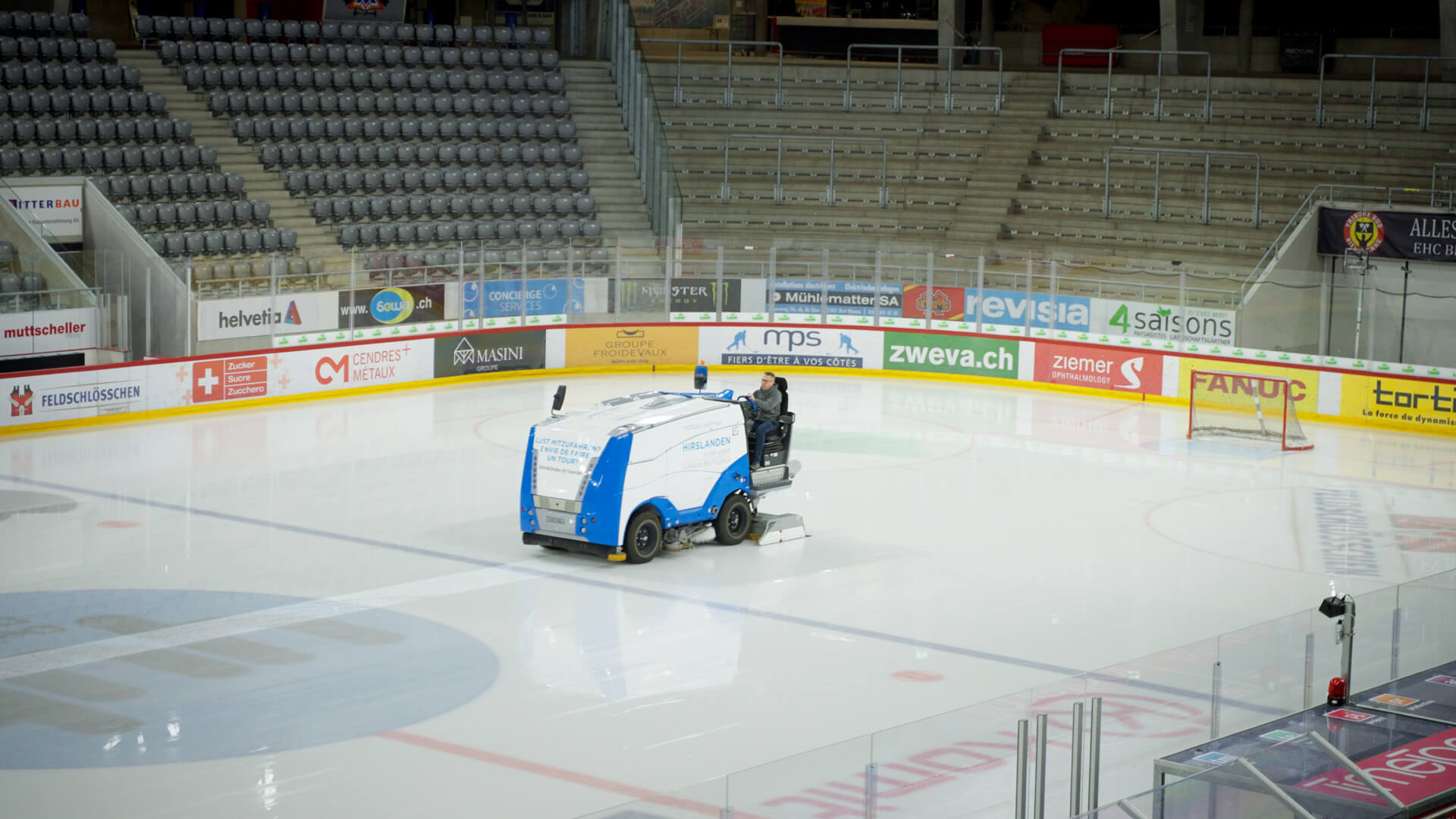 Der Alltag vom Leiter Eismeister in der Tissot Arena: Eine Person steuert die Eismaschine über das leere Eisfeld der Halle, umgeben von unbesetzten Zuschauerrängen.