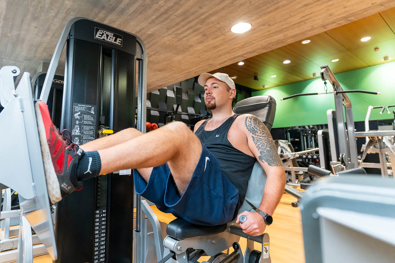 Ein Mann in Sportkleidung benutzt in einem Fitnessstudio eine Beinpresse und drückt im Sitzen mit den Beinen auf die Fußplatte.