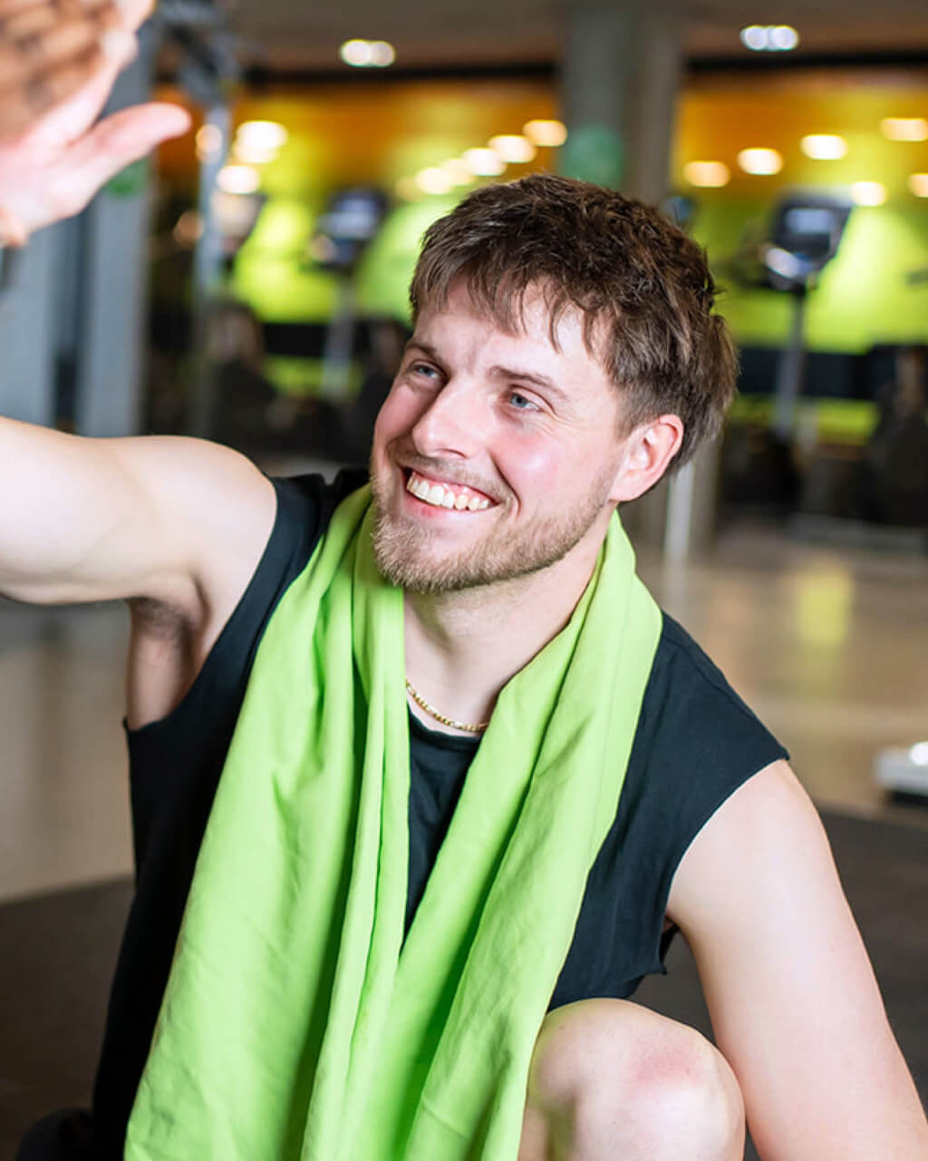 Ein lächelnder Mann in Trainingskleidung mit einem grünen Handtuch um den Hals gibt in einem Fitnessstudio ein High Five.