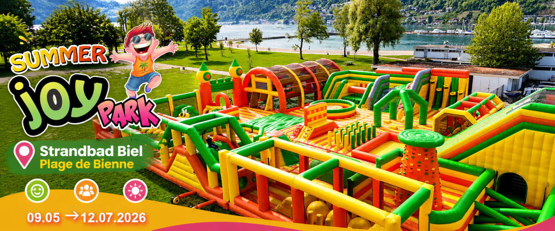 Grosser bunter aufblasbarer Hindernisparcours auf einer Wiese in der Nähe eines Sees, mit Veranstaltungshinweisen für den Summer Joy Park im Strandbad Biel vom 9. Mai bis 12. Juli 2026.